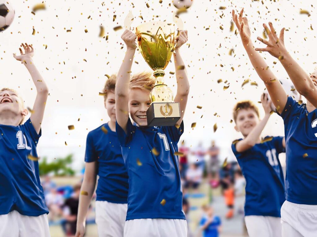 Champion youth soccer team with winning trophy. Boys football team celebrating victory in school competition by rising up golden cup